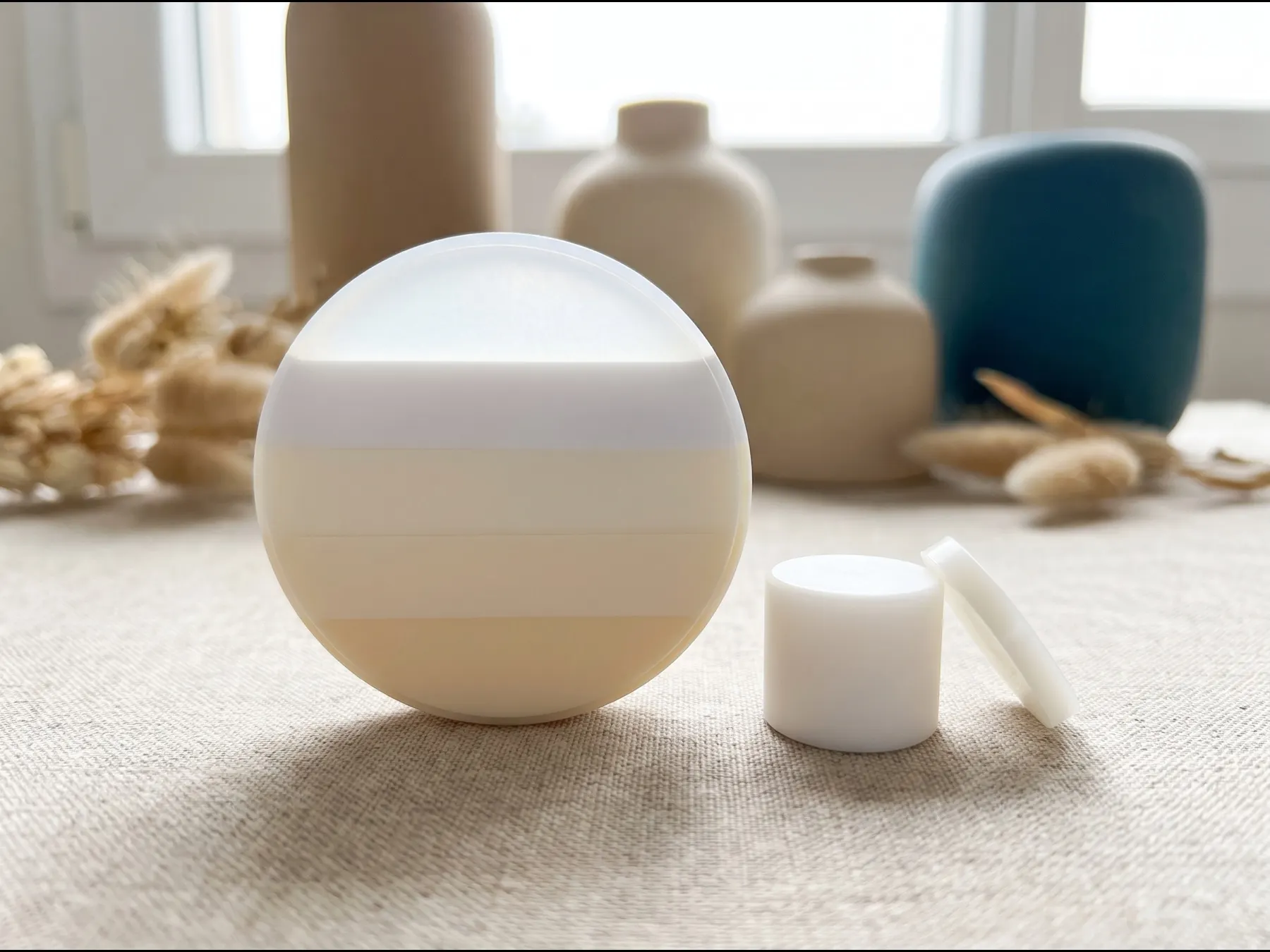 A multilayer zirconia disc on its edge showing five bands from warm ivory to translucent white, next to a single-shade lithium disilicate ingot and a thin translucent wafer